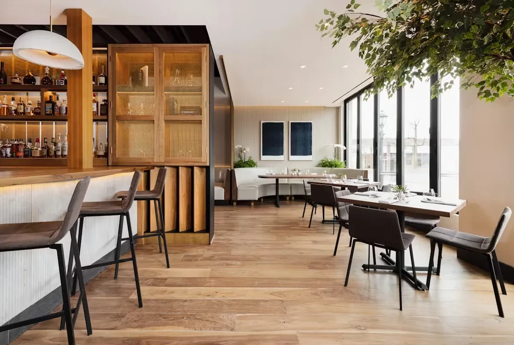 A modern restaurant interior with a bar, dining tables, and large windows.