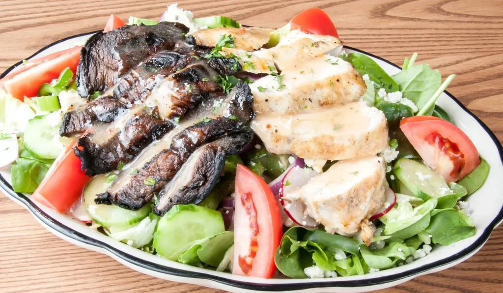 Grilled chicken and mushroom salad with vegetables and dressing on a plate.