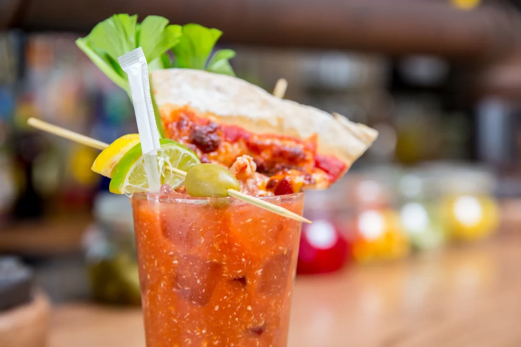 Close-up of a Bloody Mary garnished with pizza, celery, lime, and olive.