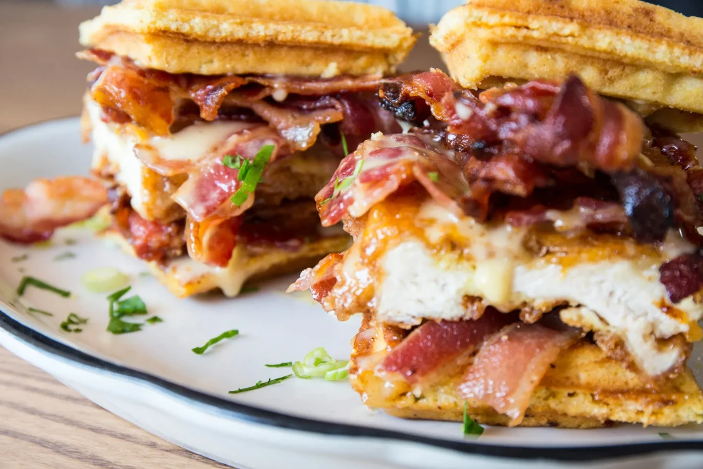 Two waffle sandwiches filled with bacon, chicken, melted cheese, and sauce.