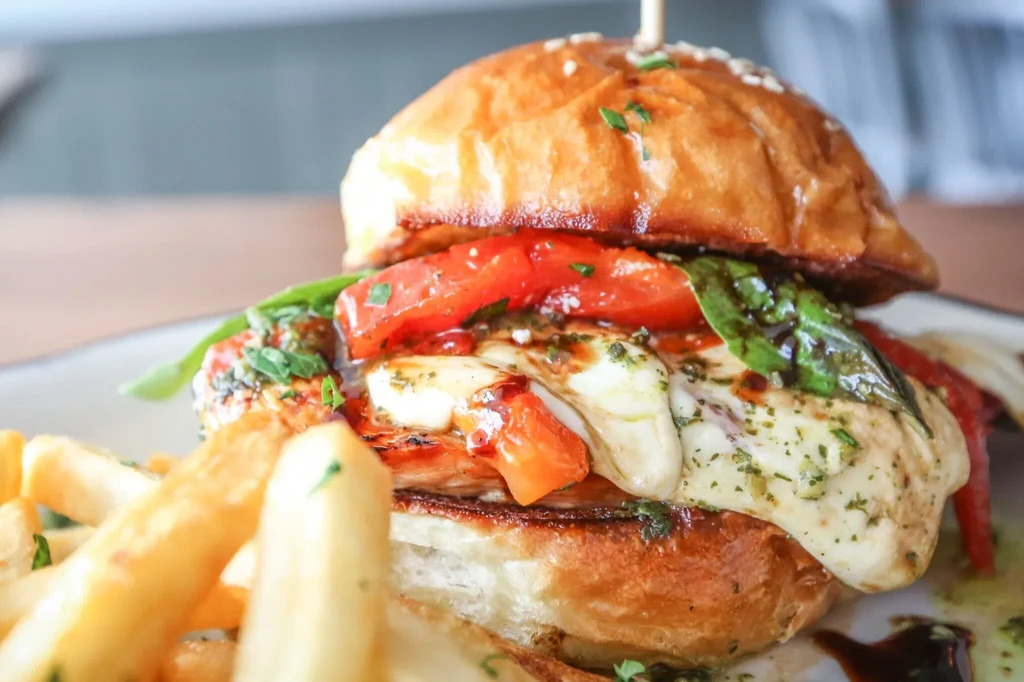 Chicken burger with melted cheese, tomato, basil, and fries.