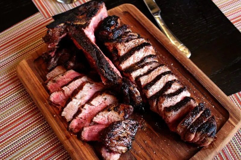 A T-bone steak, sliced, served on a wooden board.