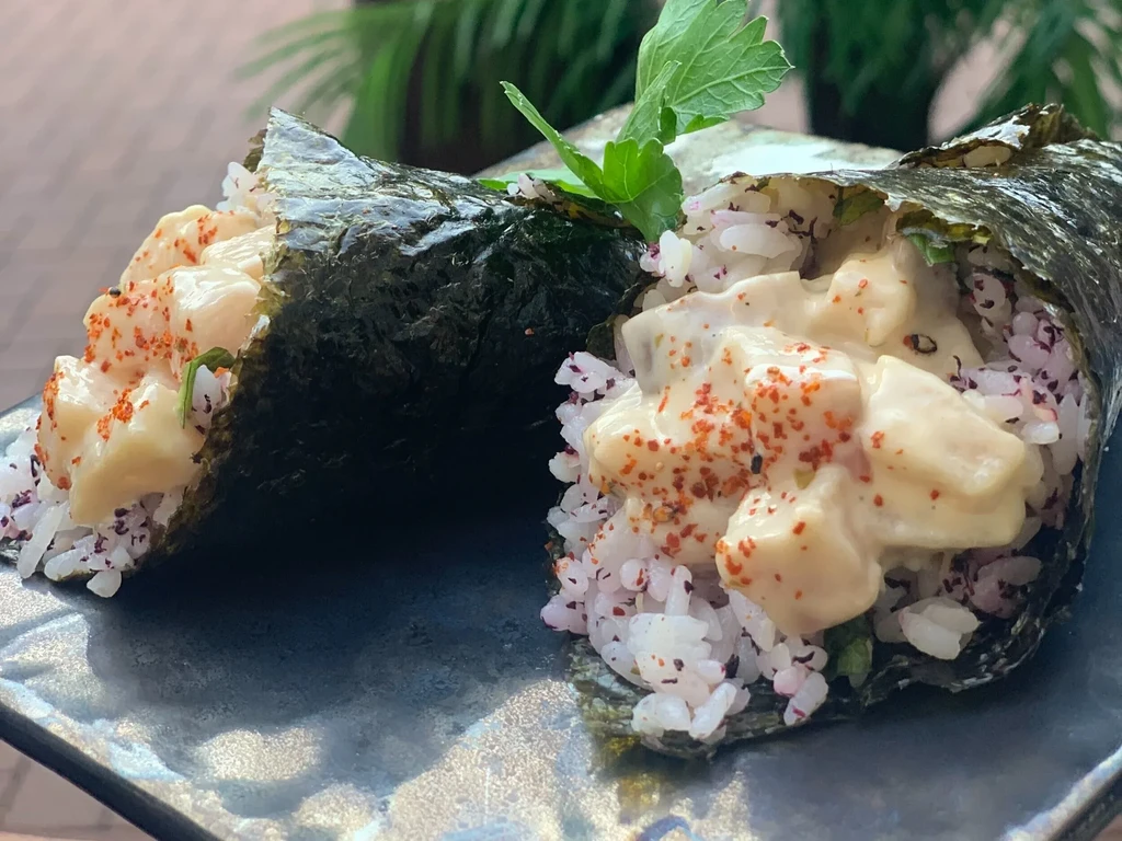 Two temaki sushi rolls, filled with rice, fish, and creamy sauce.