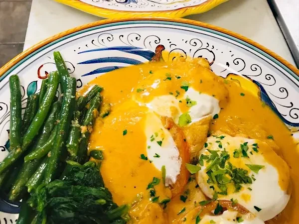 Chicken in orange sauce with green beans and spinach on a decorative plate.