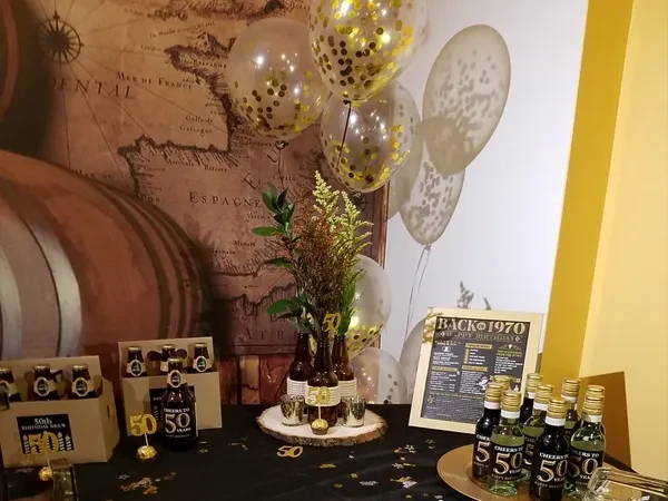 A black table set for a 50th birthday celebration with drinks and balloons.