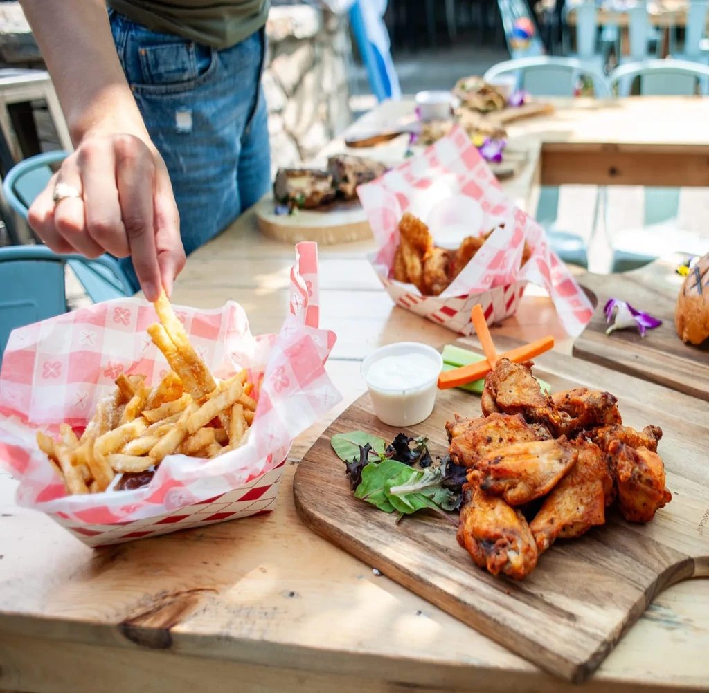 A person's hand reaches for a fry from a basket of fries.