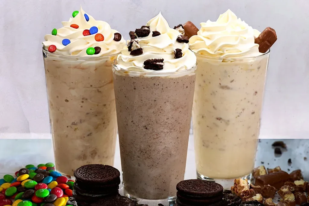 Three milkshakes topped with whipped cream, M&M's, and cookies.