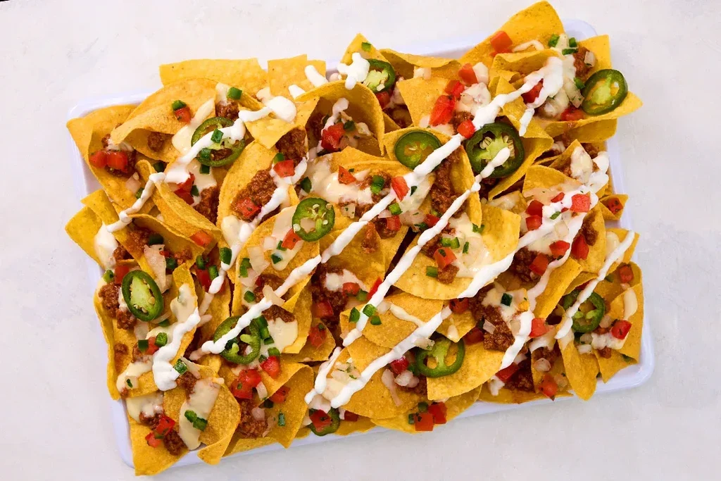 A tray of nachos with meat, cheese, salsa, sour cream, and jalapeños.