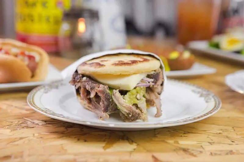 Arepa with meat, cheese, and vegetables on a white plate.