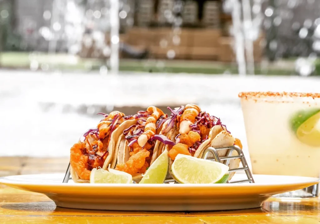 Shrimp tacos with red cabbage and lime, next to a margarita.