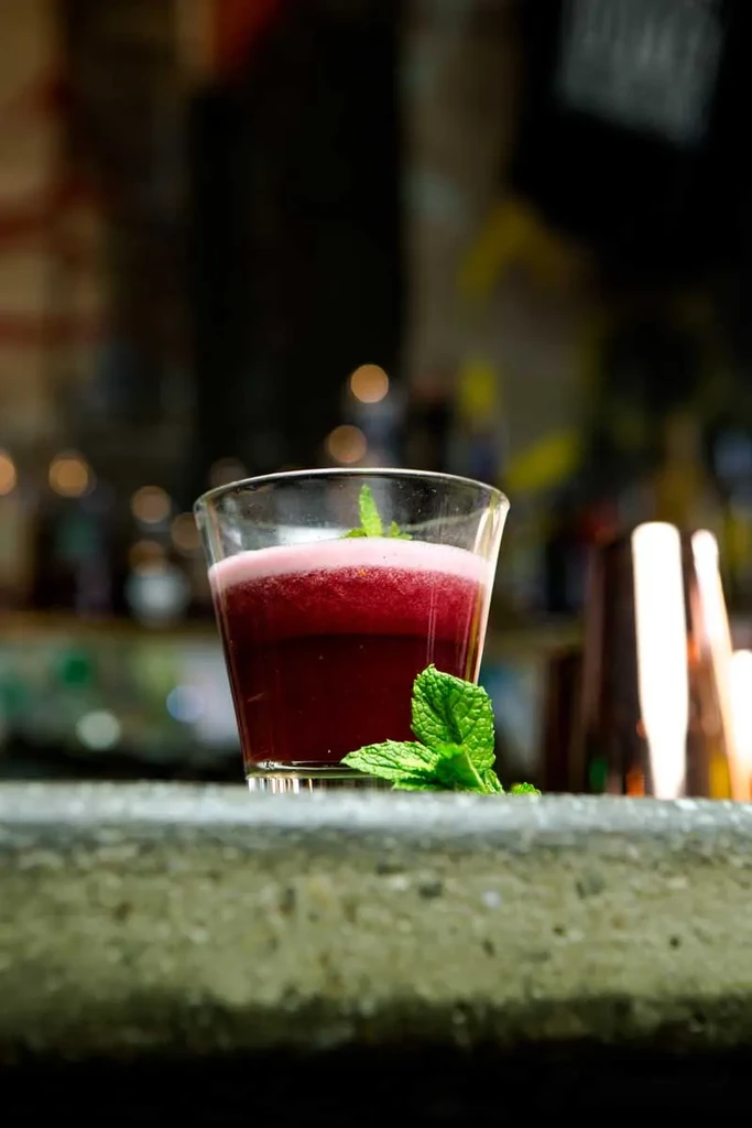 A glass of red foamy drink with mint leaves on a counter.