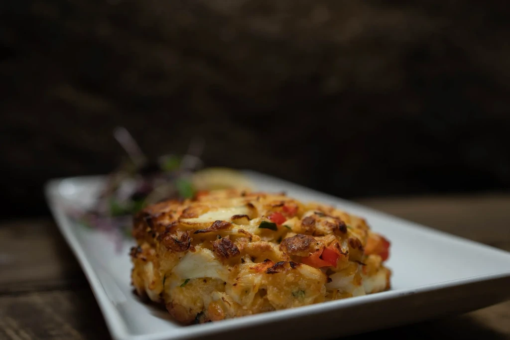 A golden-brown baked crab cake with vegetables on a white plate.
