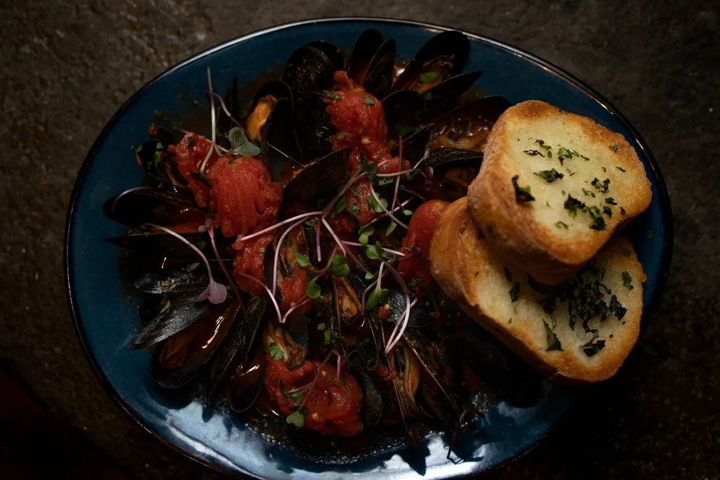 Top-down view of mussels in tomato sauce with toast on a blue plate.