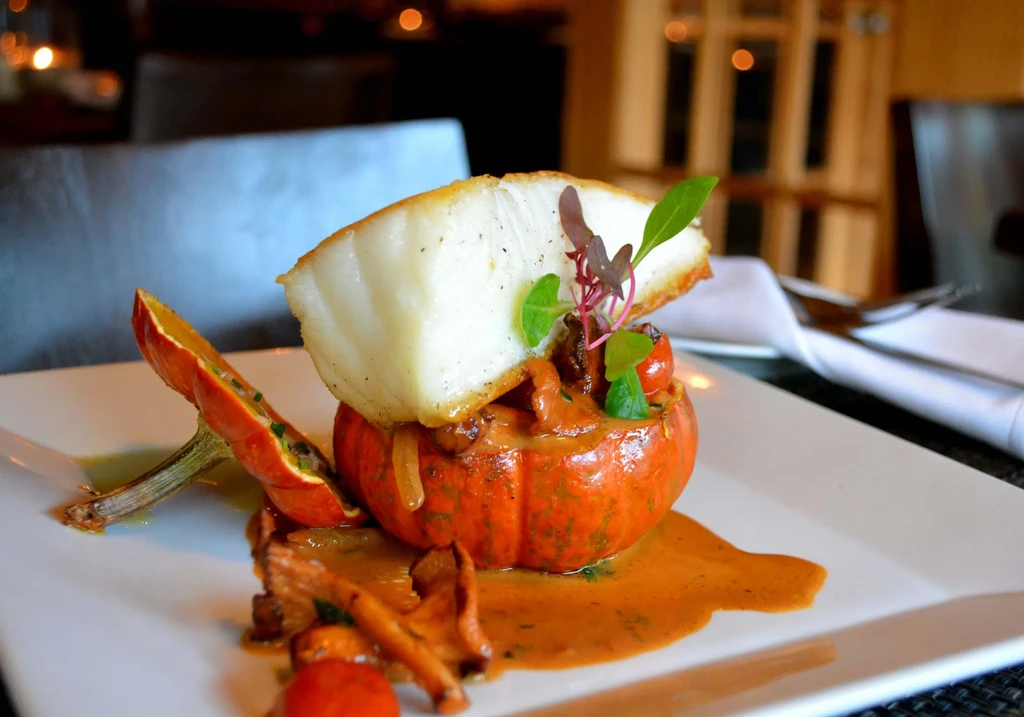 Pan-seared fish on a pumpkin filled with stew, on a white plate.