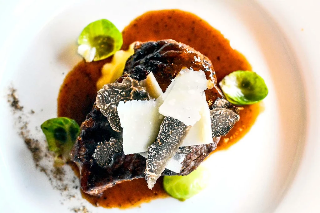 Close-up of a meat dish with truffles, cheese, and a brown sauce.