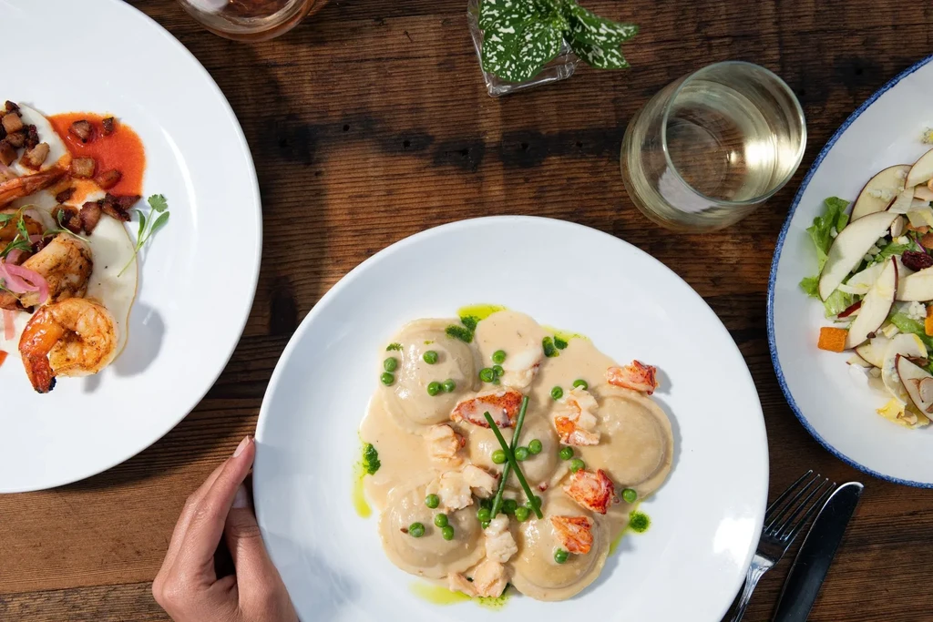 Overhead view of three plates of food and a drink on a wooden table.