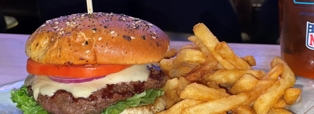A close-up shot of a cheeseburger, fries, and a beverage.