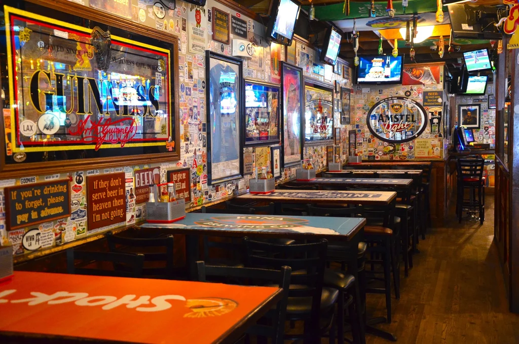 An empty bar with tables, chairs, and walls covered in stickers and signs.