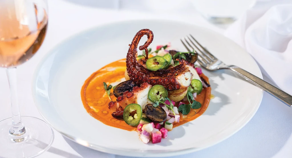 Plate of octopus with sauce, vegetables, and a glass of rosé.