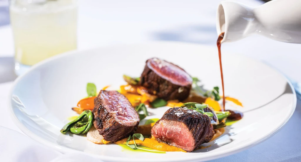 Red sauce is poured onto three medium-rare steaks and vegetables.