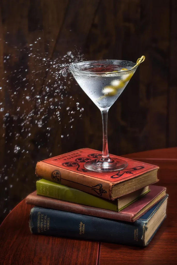 Frosty martini with olives splashes water atop antique books.