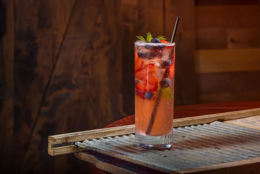 Pink berry and mint drink in a glass on a rustic surface.