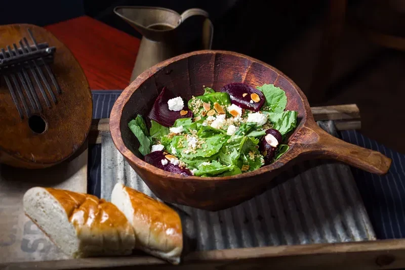 Rustic still life: fresh salad, bread, kalimba, brass pitcher.