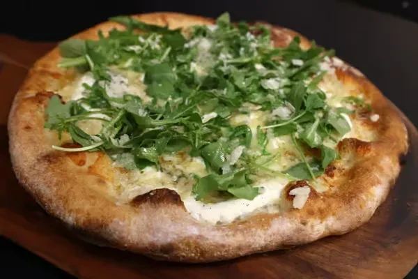 Close-up of a white sauce pizza with arugula and Parmesan on a board.
