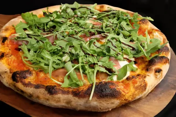 Wood-fired pizza with arugula, prosciutto, mozzarella, and balsamic glaze.