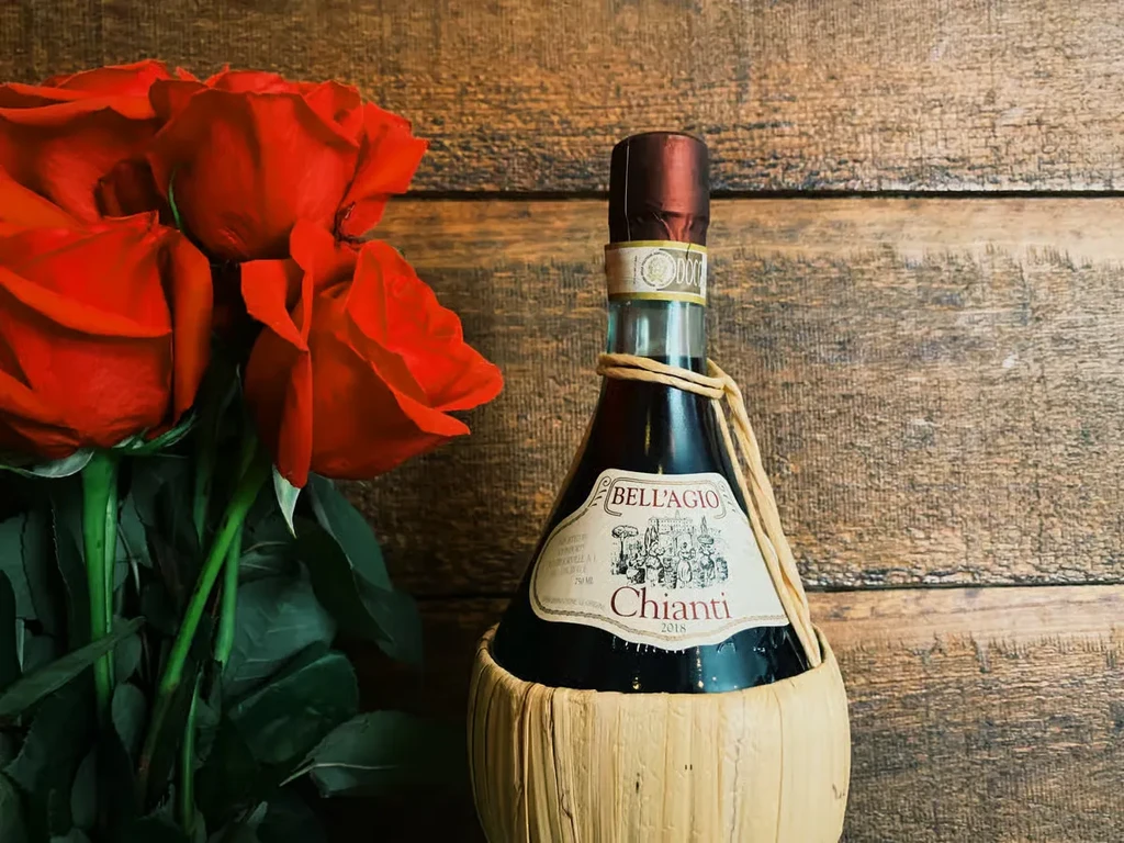 2018 Bell'Agio Chianti fiasco and red roses on dark wood.