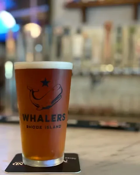 Amber beer pint with "Whalers Rhode Island" logo in a blurred bar.