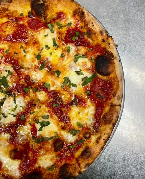 Baked pizza with golden crust, melted cheese, tomato sauce, and fresh herbs.