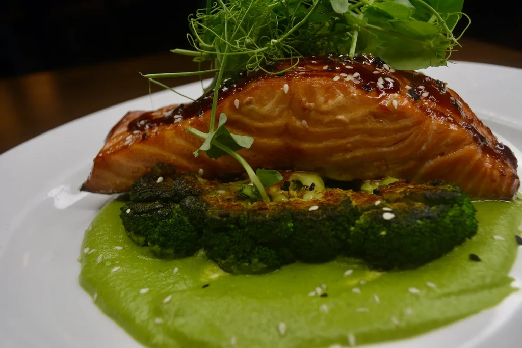 Teriyaki salmon with broccoli and green purée on a white plate.