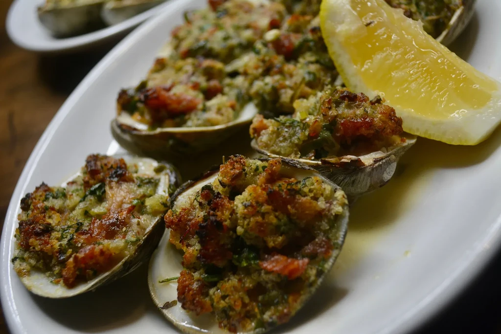 A plate of baked clams with breading and a lemon wedge.