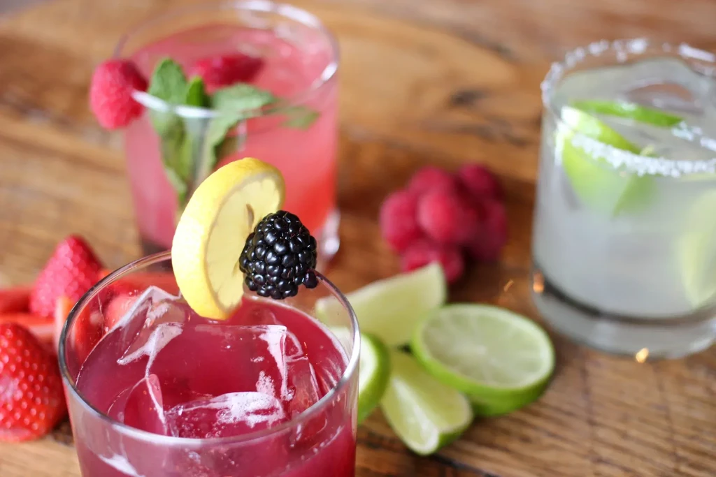 Three colorful drinks with fruit garnishes on a wooden table.