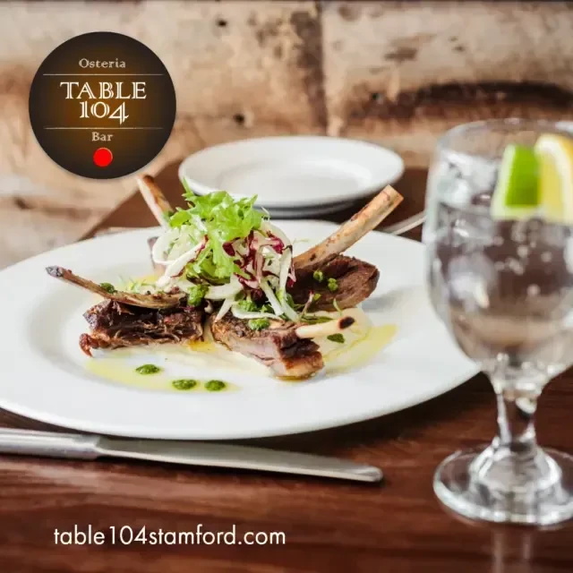 Rack of lamb with salad, a knife, and a drink.