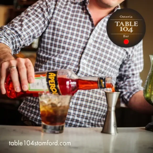 Bartender pours Aperol from a bottle into a measuring jigger.