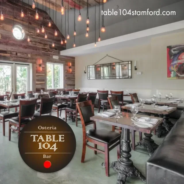 An empty restaurant with dark tables and chairs under hanging industrial lights.