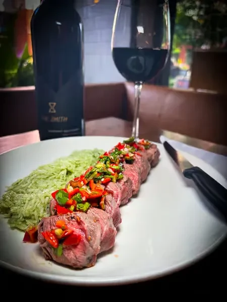 Sliced steak with chimichurri, green rice, wine, and a knife.