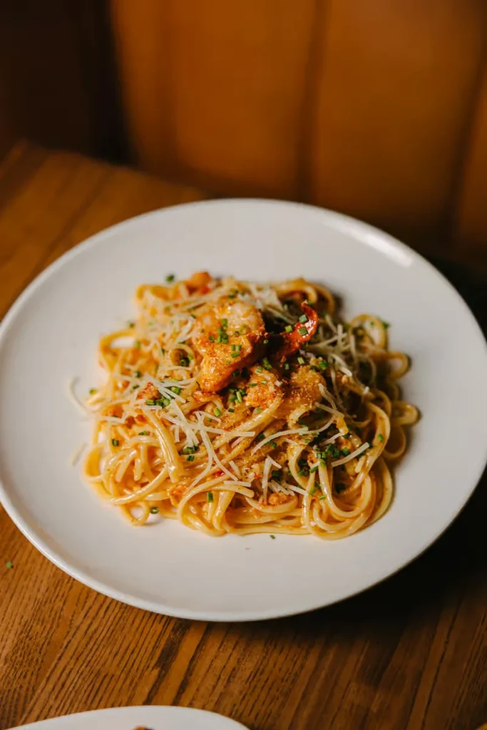 Plate of lobster linguine pasta topped with cheese and chives.