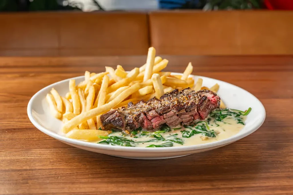 Steak frites with creamed spinach on a white plate.