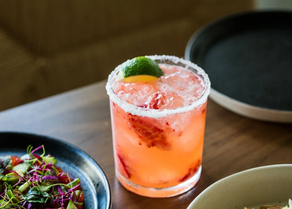 Pink cocktail with ice, lime, orange, and a salt rim.
