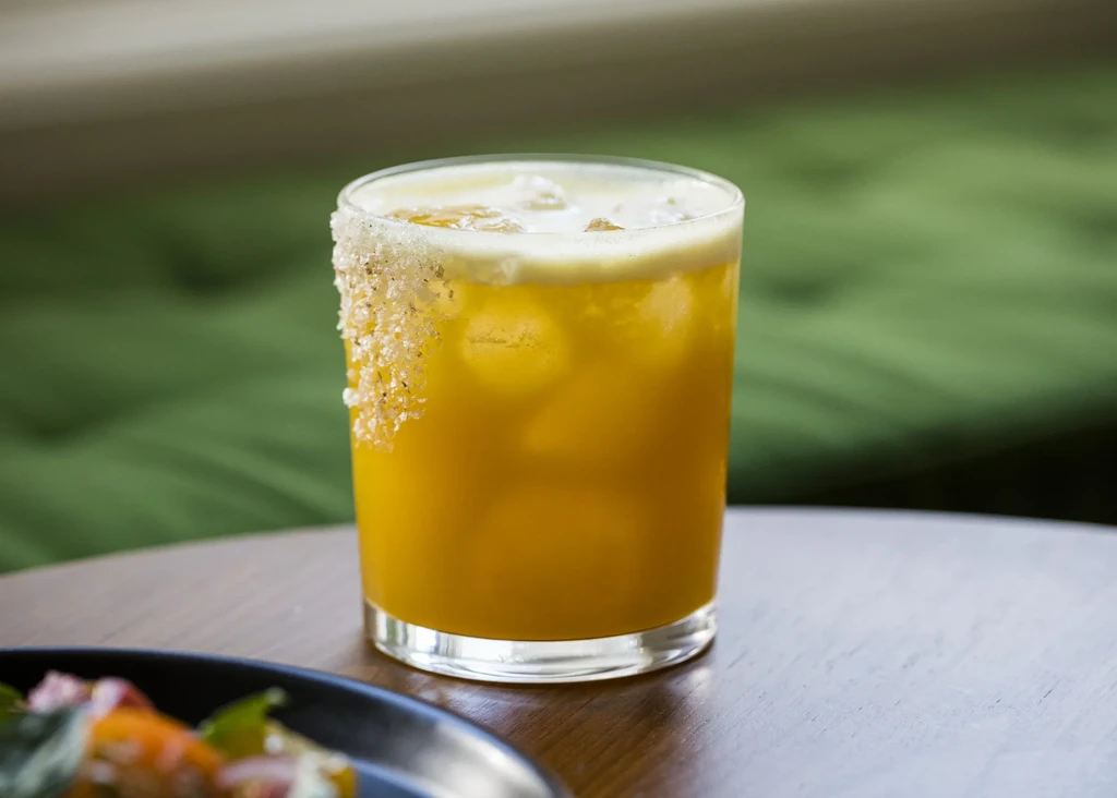 A tall glass of orange liquid with ice and a salt rim.
