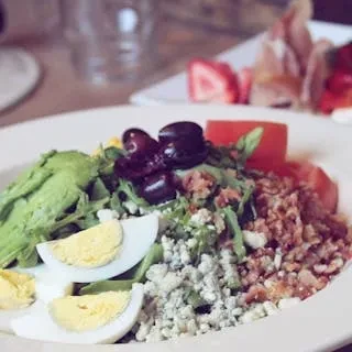 A close-up shot of a gourmet salad with avocado, eggs, and bacon.