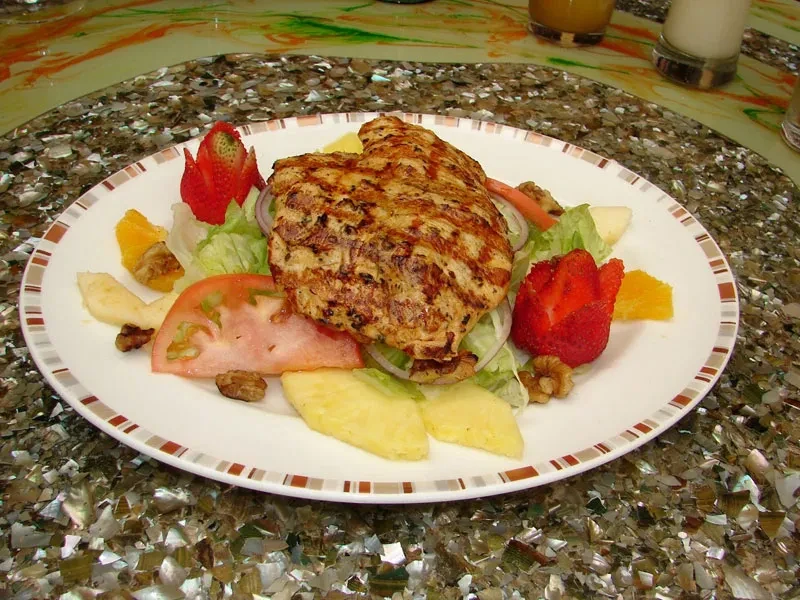 A grilled chicken breast salad with fruit and nuts on a white plate.