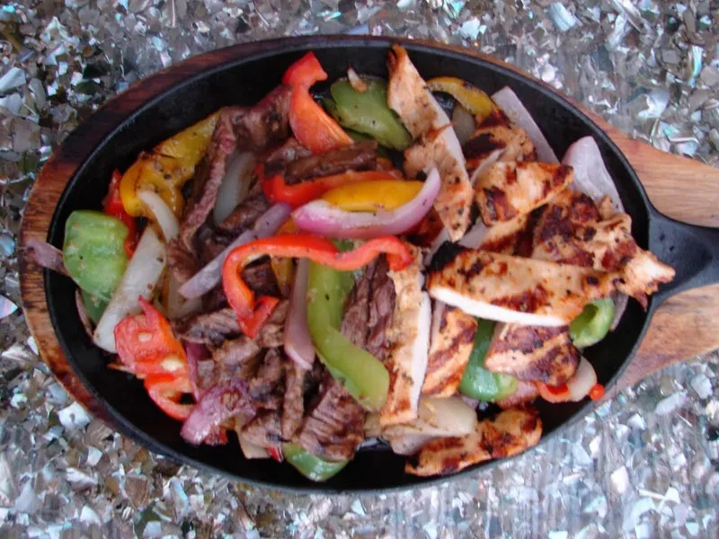 Sizzling fajitas with chicken, beef, onions, and bell peppers in a cast-iron skillet.