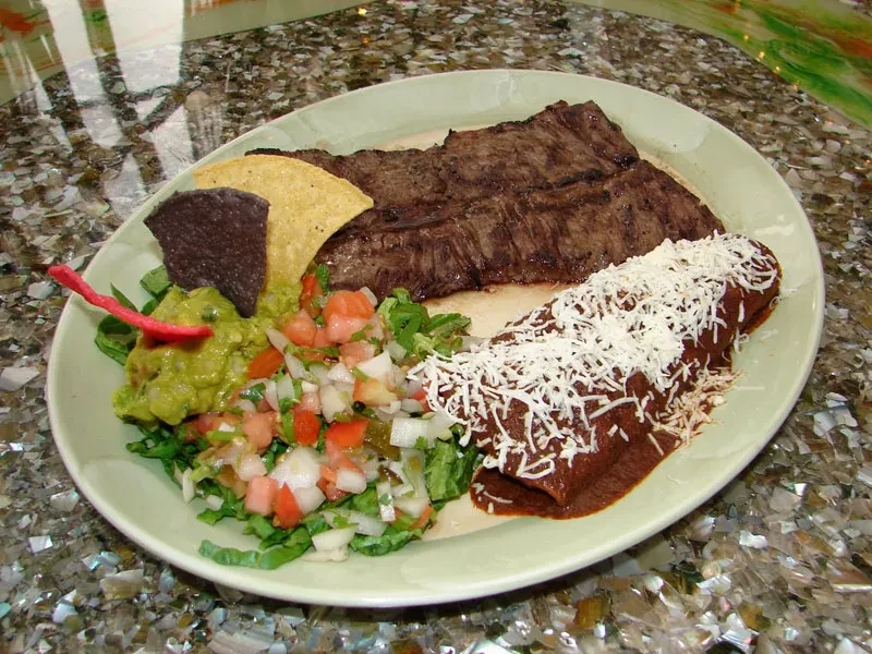 A plate of steak, enchilada, guacamole, salsa, and tortilla chips.