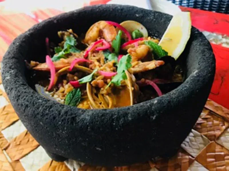Molcajete dish with shrimp, clams, red onions, cilantro, and lemon.