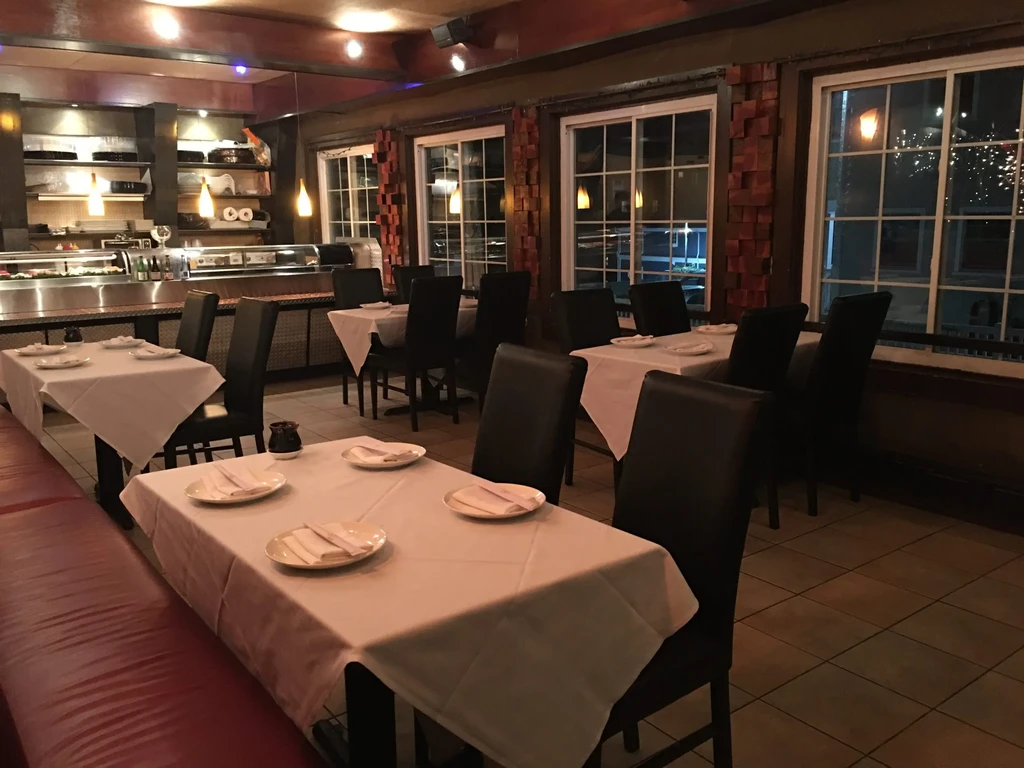 Empty restaurant with white tablecloths, dark chairs, and sushi counter.