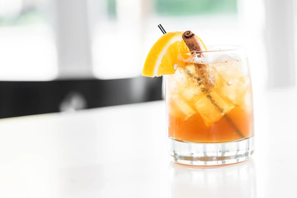 An iced cocktail garnished with an orange slice and cinnamon stick.